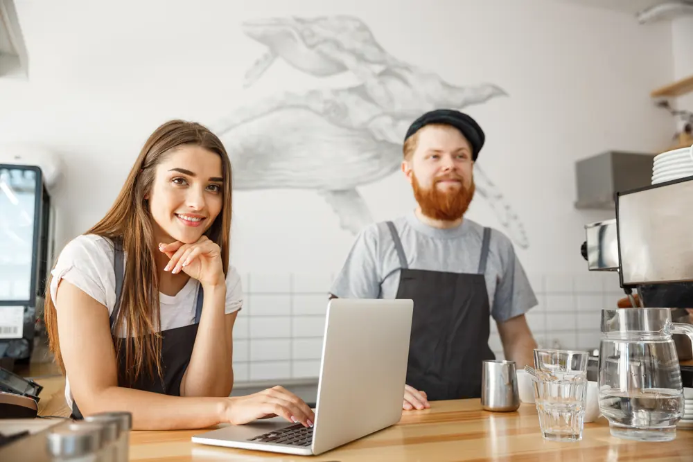 Dois atendentes de uma cafeteria usando um notebook no balcão